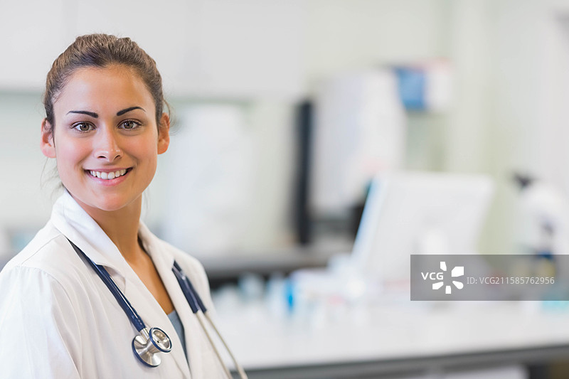 穿着白色实验室外套的女医生佩戴听诊器，在实验室中查看监视器，留有空白空间图片素材