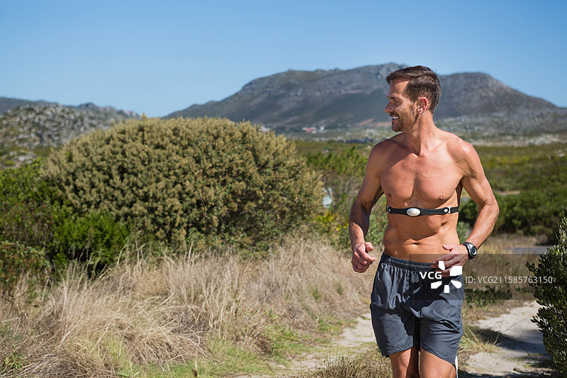 男性慢跑者沿小径跑步，佩戴心率监测胸带和运动手表，留有空白空间图片素材