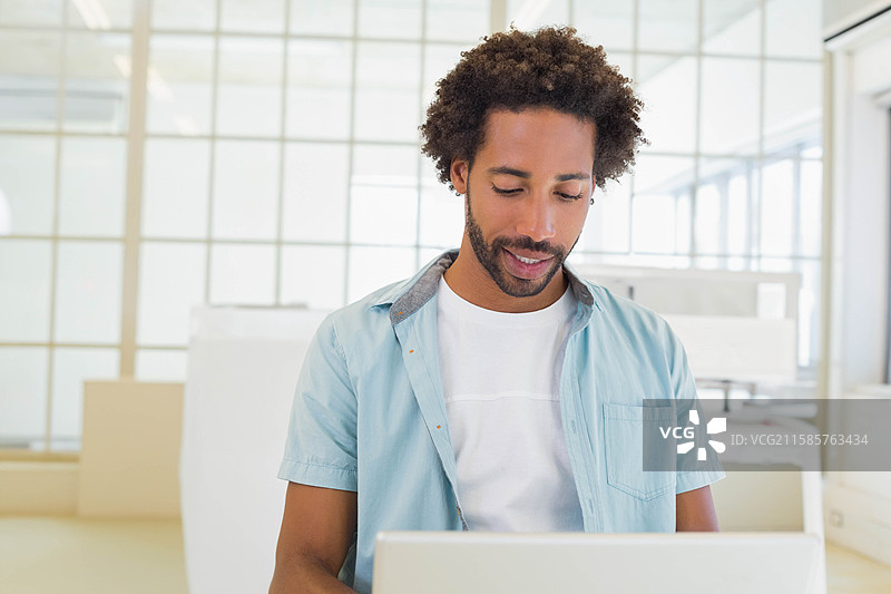 中年非裔美国男性穿着浅蓝色衬衫，在现代办公室桌子上使用笔记本电脑。图片素材