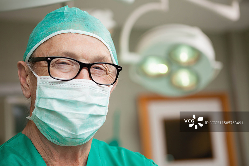 穿着绿色手术服和黑框眼镜的外科医生在手术室的灯光下，专注于监视器工作。图片素材