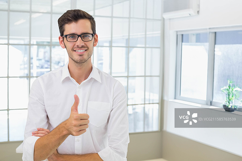 男办公室工作人员站在办公室的玻璃隔断后，戴着眼镜，穿着白衬衫。图片素材