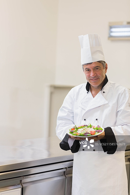 男厨师在专业厨房中举着一盘新鲜沙拉面向镜头，留有空白空间图片素材