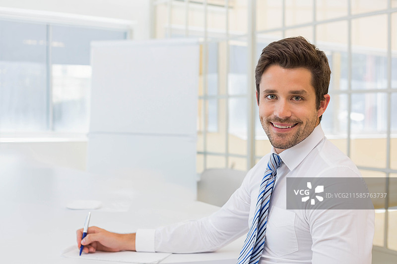 男性专业人士坐在桌子旁，手持蓝色钢笔，正在审阅工作空间中的文件，留有空白区域。图片素材