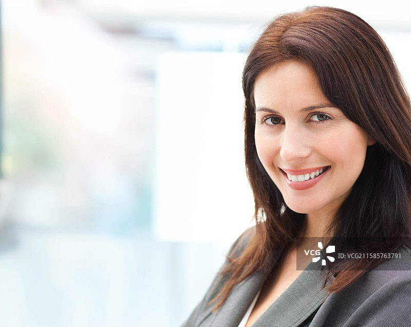 中年女性微笑着看向镜头，穿着灰色西装外套和浅色衬衫，背景留有空白。图片素材