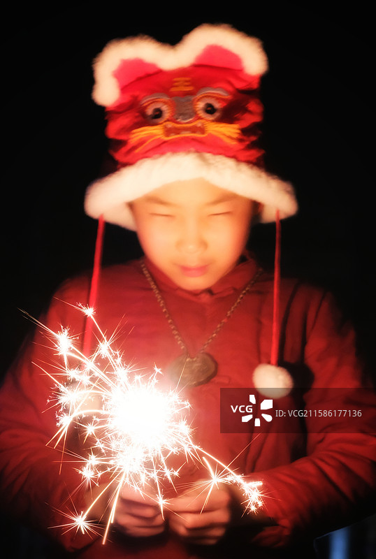 新春春节新年。黑夜戴虎头帽玩儿仙女棒的中国小男孩图片素材