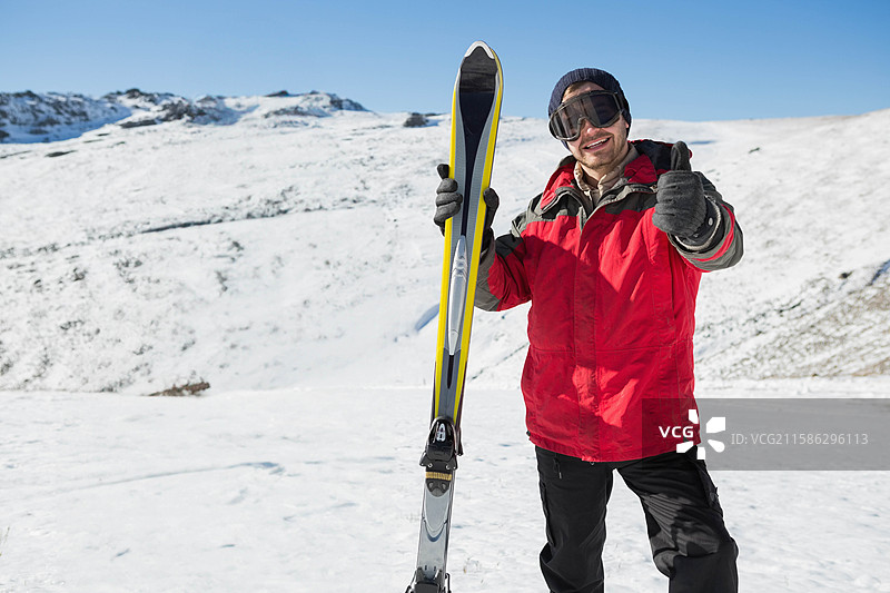 独自滑雪者站在雪覆盖的山坡上，蓝天清澈，手持直立的滑雪板图片素材
