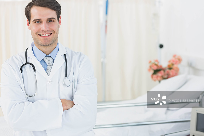 男医生站在病房的病床旁，展示听诊器和鲜花，留有空白空间。图片素材