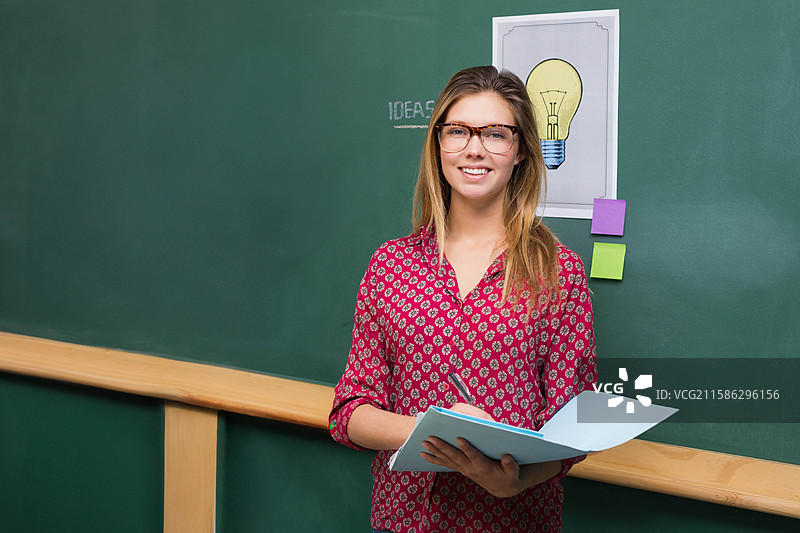 女教师在黑板前写笔记，旁边有灯泡海报，留有空白空间图片素材