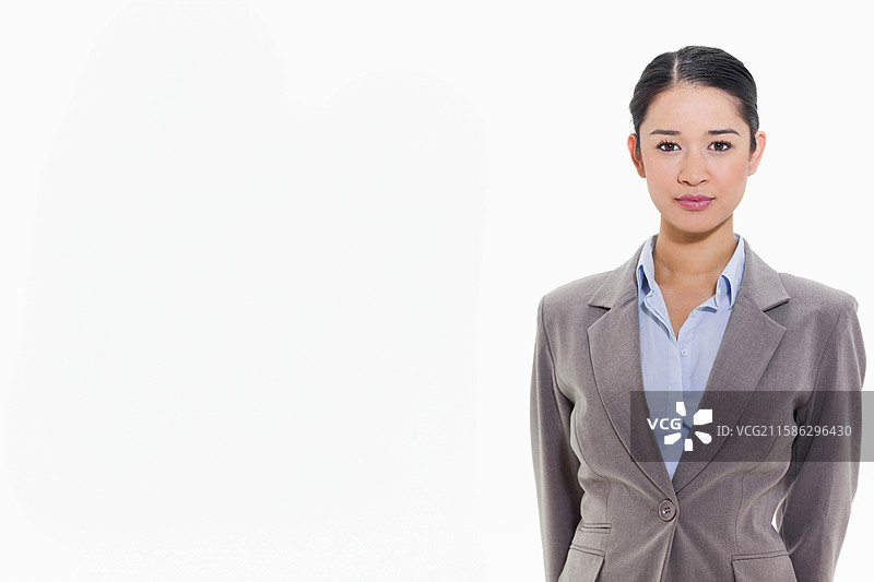 身穿灰色西装和蓝色衬衫的亚洲女性站在白色背景前，留有空白空间。图片素材