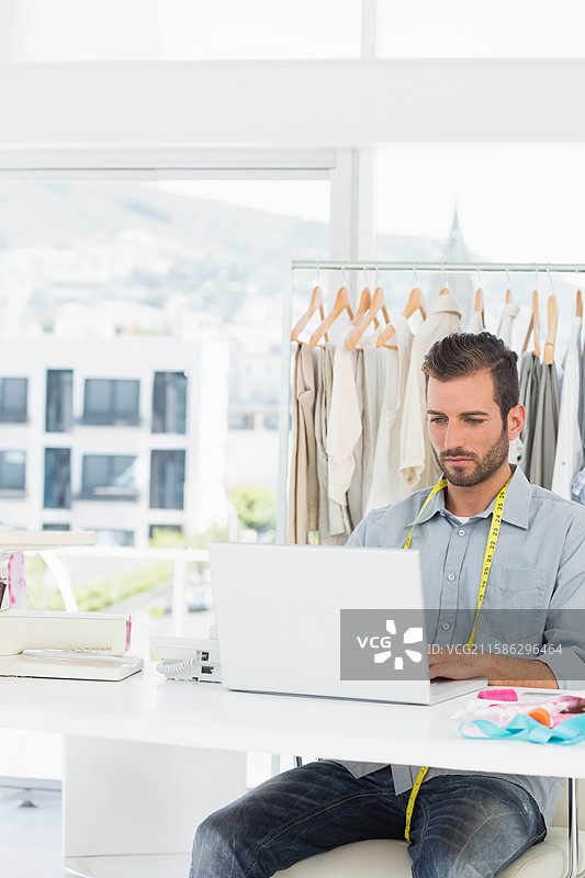 西班牙裔男子坐在工作室桌子前，使用笔记本电脑和卷尺，留有空白空间图片素材