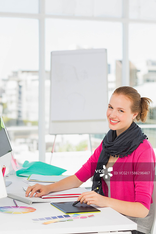 在窗边的桌子上，女性正在使用数字绘图板工作，旁边有电脑显示器，留有空白空间。图片素材