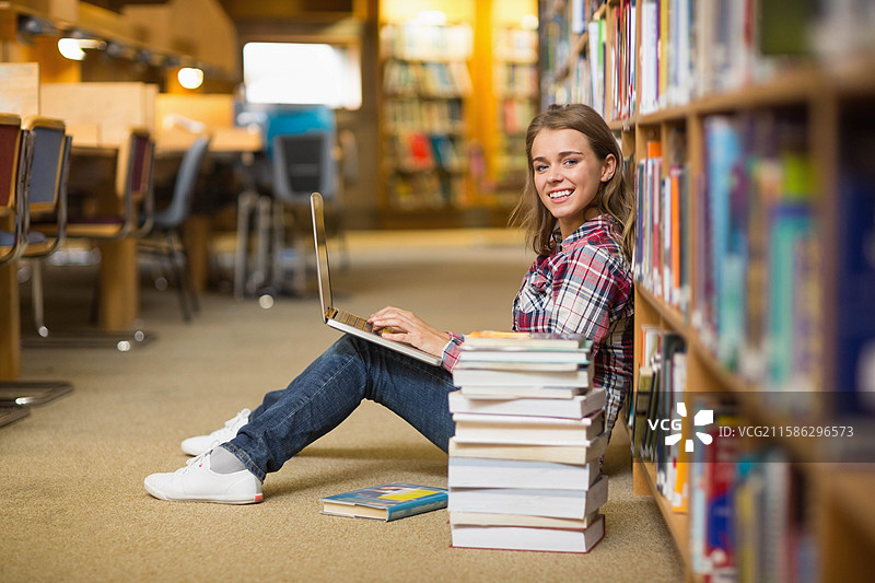 白人青少年学生坐在图书馆，靠在书架上使用笔记本电脑，周围有书籍，留有空白空间图片素材