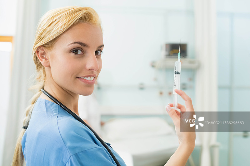 女护士佩戴听诊器，手持并检查注射器，站在诊所的床边，留白空间。图片素材