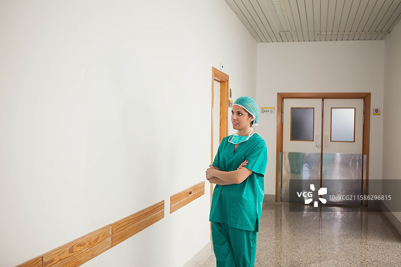 穿着绿色手术服和口罩的女性站在医院走廊的扶手旁，留有空白空间图片素材
