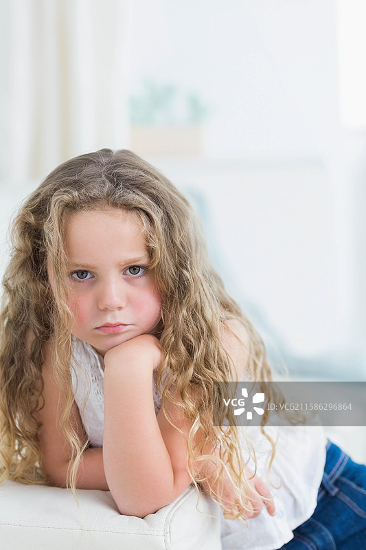 女孩坐在客厅的沙发上，靠着手托着下巴，旁边有一盆植物和抱枕。图片素材