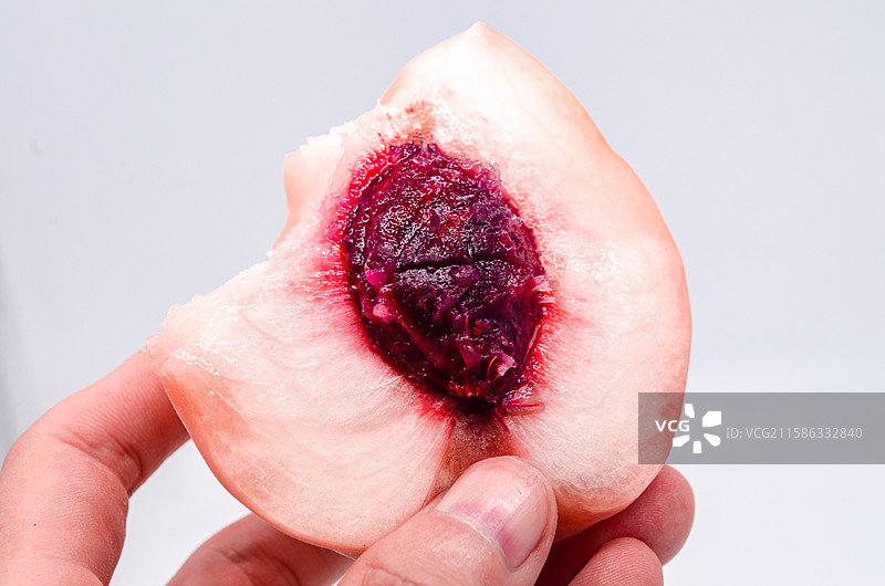 中国水果饮食产业影棚拍摄主题，一个人拿着咬过的粉红色的肥城桃子水蜜桃毛桃横截面桃核，室内无人图像摄影图片素材