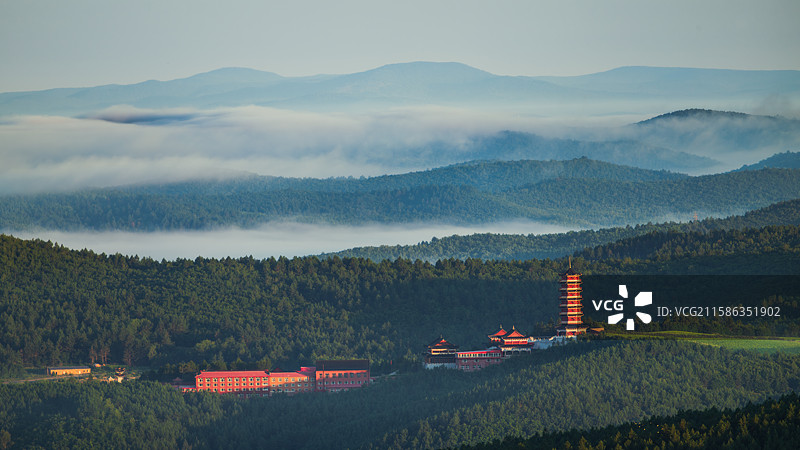 清晨日出时分，晨雾在大兴安岭起伏的山间缭绕，远眺加格达奇金刚圣寺寺院与佛塔，被阳光照亮，水墨画风格图片素材