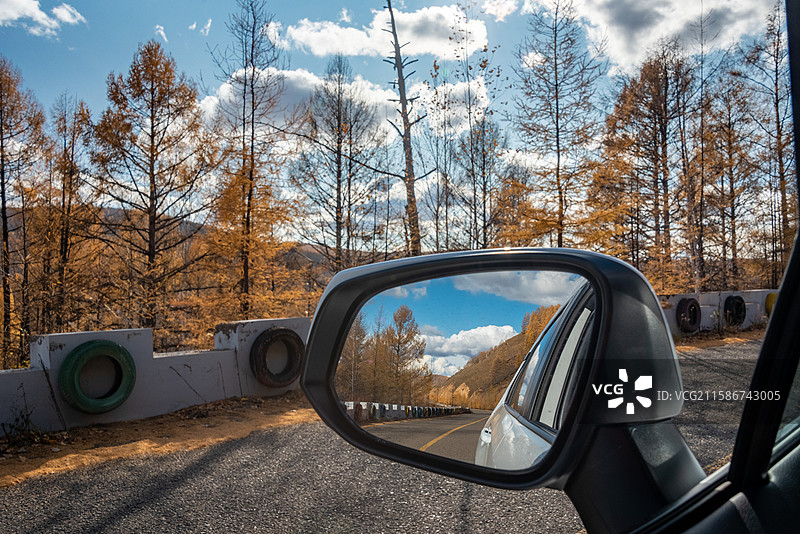 后视镜视角，莫尔道嘎秋日乡村道路自驾游，金黄树木与蓝天白云相映。图片素材