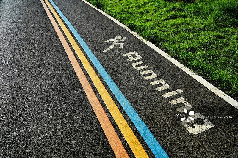 绿意盎然的草地旁色彩鲜明的跑步专用道与运动标识图片素材