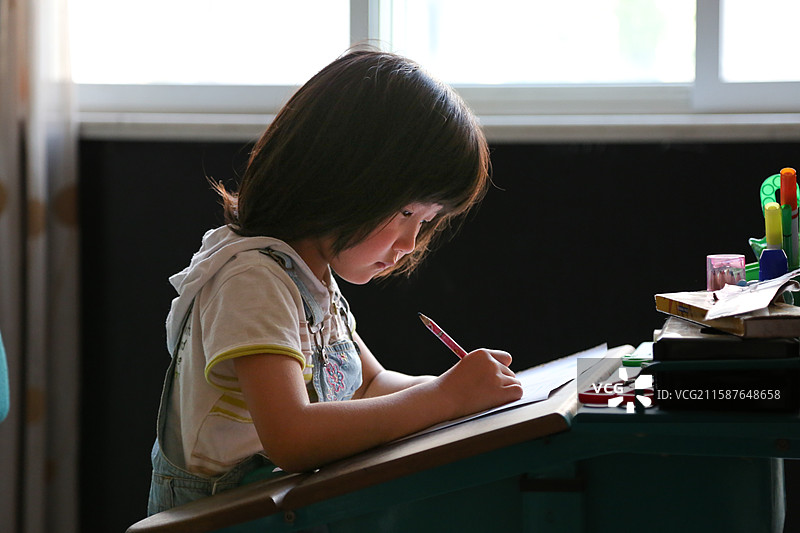 小女孩专注地在课桌上写字图片素材