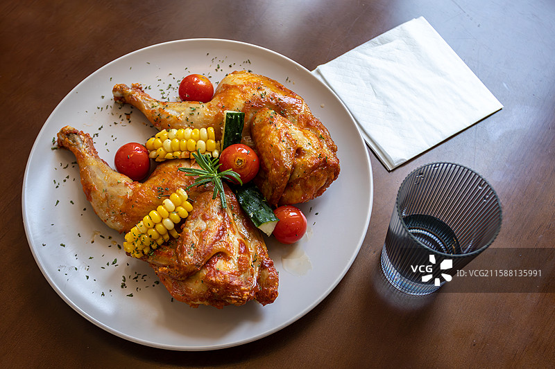 白色圆盘上的烤鸡腿配玉米番茄图片素材