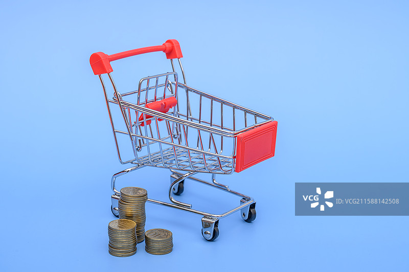 蓝色背景前的购物车和硬币购物消费概念图片素材