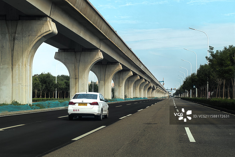 一条长长的高架桥，整齐的立柱形成延长线，一辆白色小汽车行驶在崭新的道路上图片素材