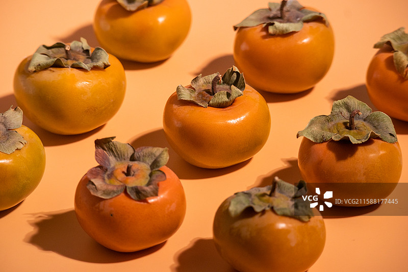 橙色背景上摆放着多个新鲜采摘的秋季柿子水果美食图片素材