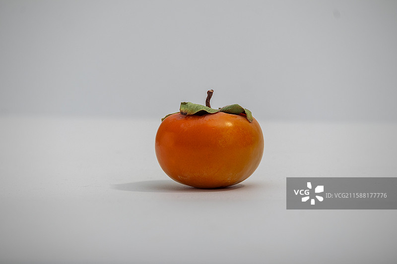 白色背景上摆放着一个新鲜采摘的柿子水果美食图片素材