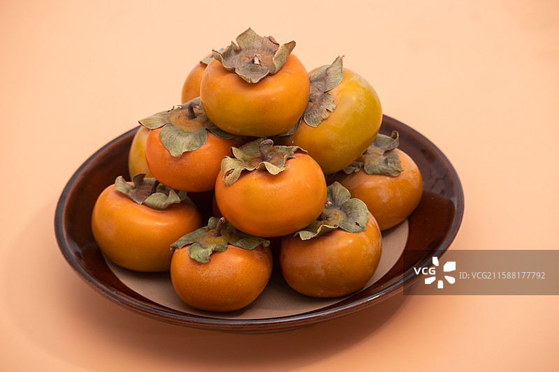 橙色背景上摆放着多个新鲜采摘的秋季柿子水果美食图片素材