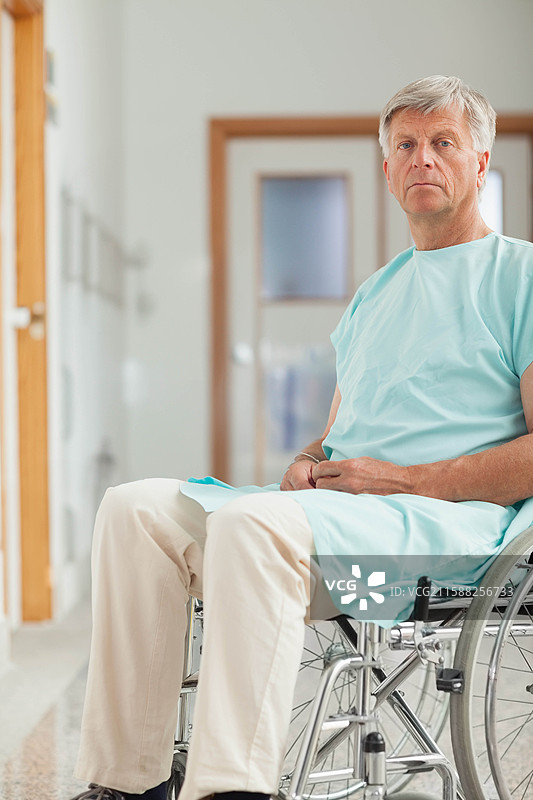 坐在轮椅上的老年男子，穿着绿色医疗长袍，位于医院走廊，留有空白空间图片素材