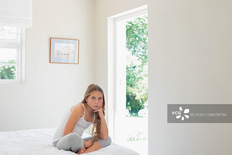 女孩坐在卧室的床上，透过敞开的门口凝视，墙上挂着装裱的艺术作品，留有空白空间。图片素材