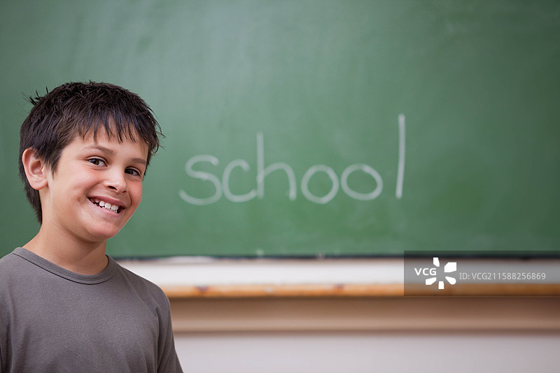 白人男孩靠在学校的木质栏杆上，旁边是绿色的黑板，上面写着“学校”这个词，有空白空间。图片素材