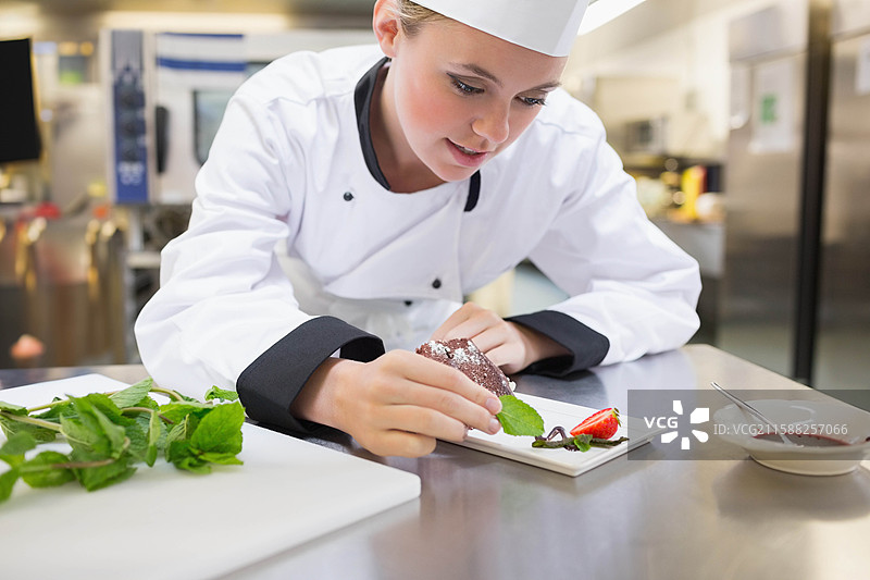 女厨师在厨房中穿着白色制服，为巧克力甜点装饰薄荷和草莓。图片素材