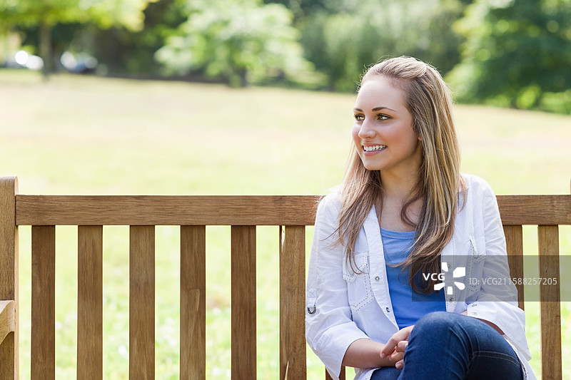 穿着休闲服的少女坐在公园的木制条凳上，背景留有空白空间。图片素材