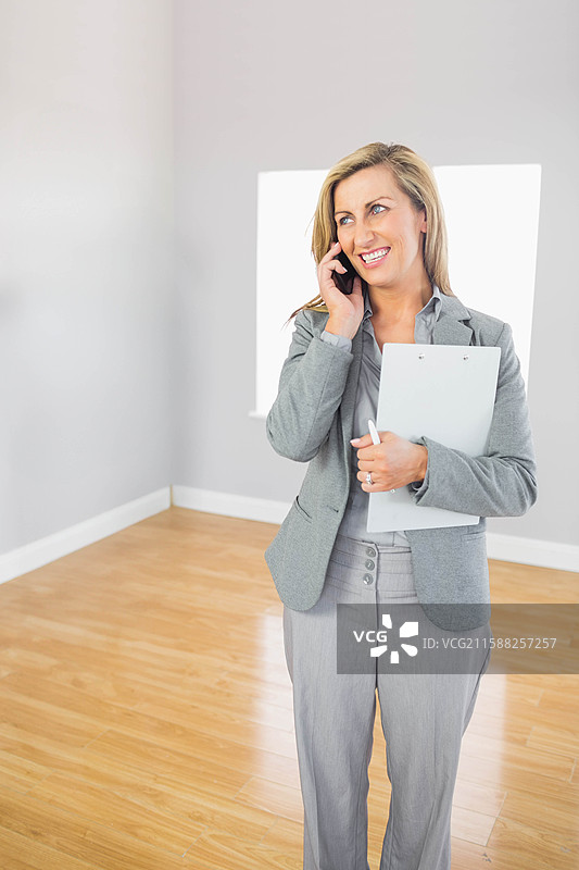 女商人在空旷的办公室里拿着夹板，同时用智能手机拨打电话，留有空白空间。图片素材
