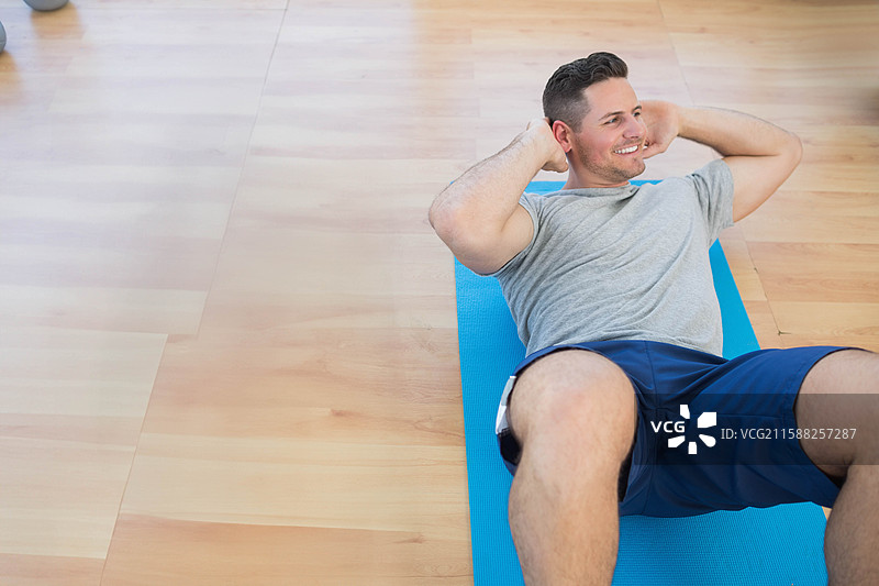 男子在家中的工作室里，使用蓝色垫子进行核心锻炼，手机固定带，留白空间图片素材