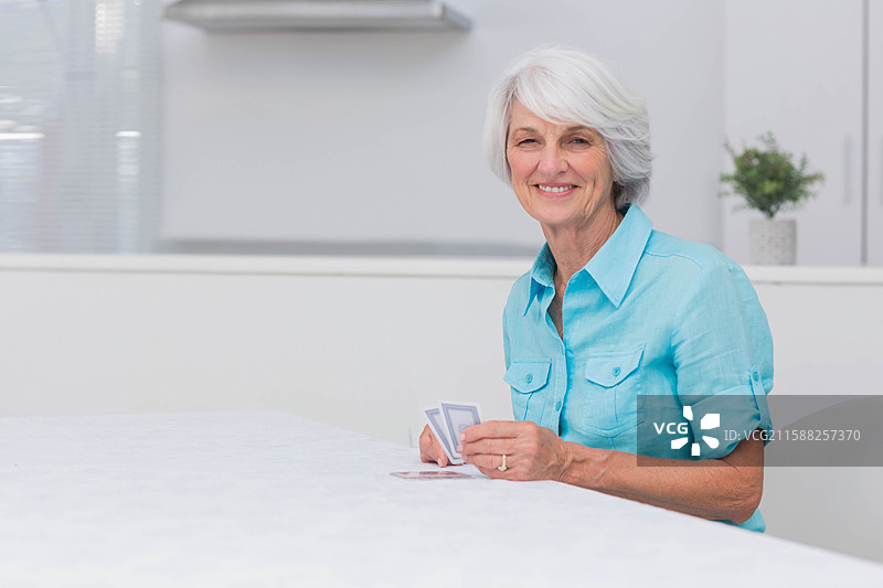 扑克牌放在厨房区域的大桌子上，旁边有百叶窗和盆栽植物。图片素材