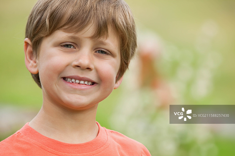 男孩站在草地上，微笑着，阳光明媚，穿着橙色圆领衫，留有空白空间。图片素材