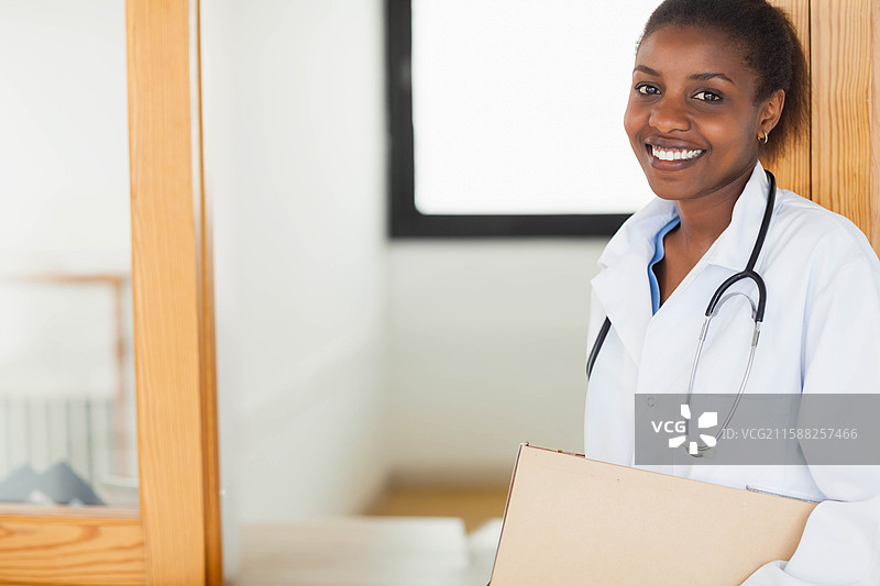 非裔美国女性医生手持纸箱，佩戴听诊器，站在窗边，留有空白空间图片素材