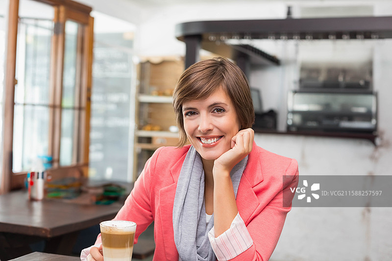 女人坐在舒适的咖啡馆里，手托着头，旁边放着拿铁咖啡杯和糖罐。图片素材