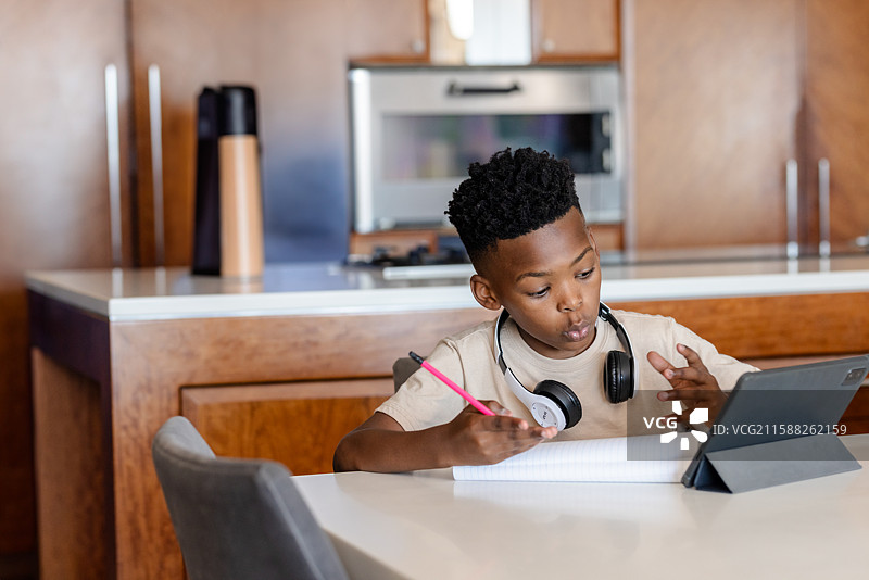 非裔美国男孩在厨房桌子上用铅笔写笔记，凝视着平板电脑，留有空白空间图片素材