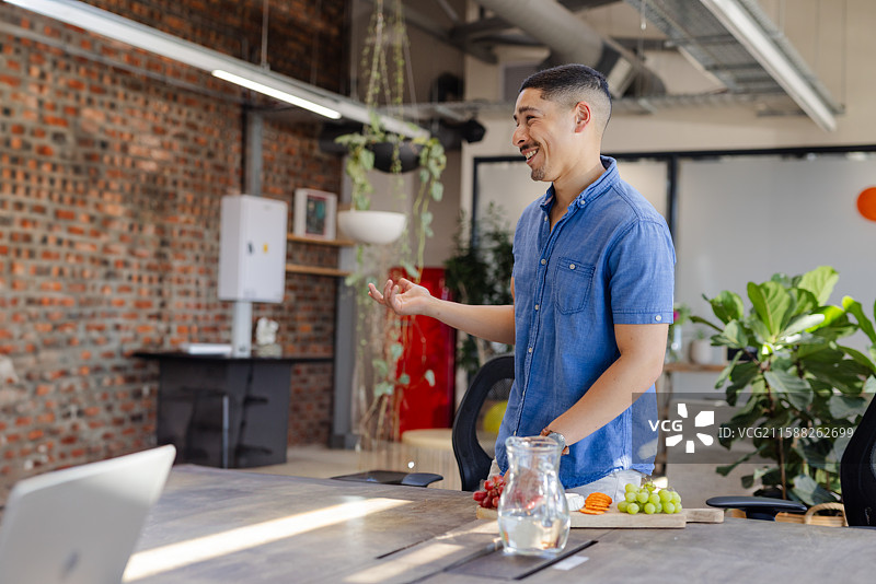 亚洲男子在会议室的桌子旁穿着牛仔衬衫，手势表达，旁边有水壶，留有空白空间图片素材