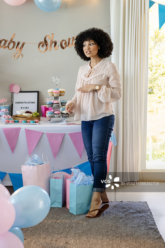 中年非裔美国女性站在家里的婴儿洗礼桌旁，桌上有杯子蛋糕和礼品袋。图片素材