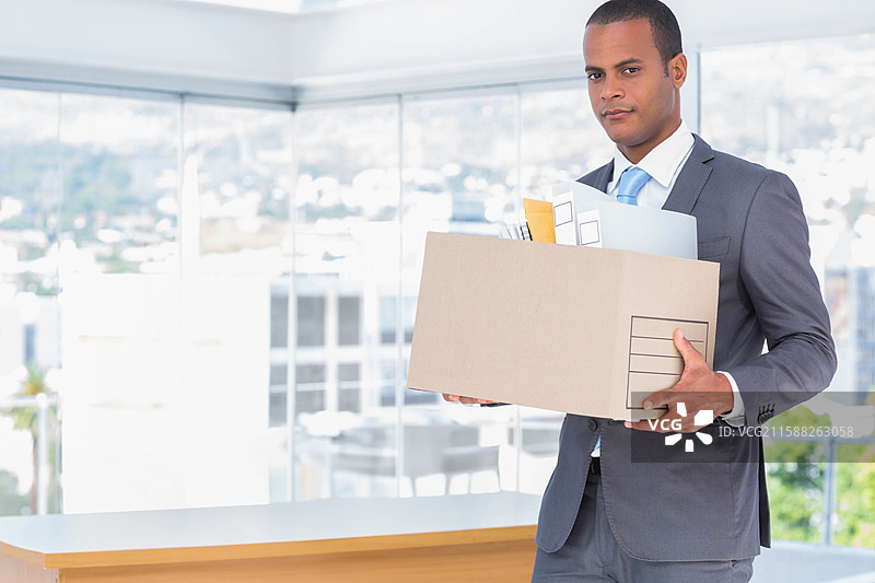 穿着西装的非裔美国男性在办公室里手持装有图纸和文件夹的盒子，留有空白空间图片素材