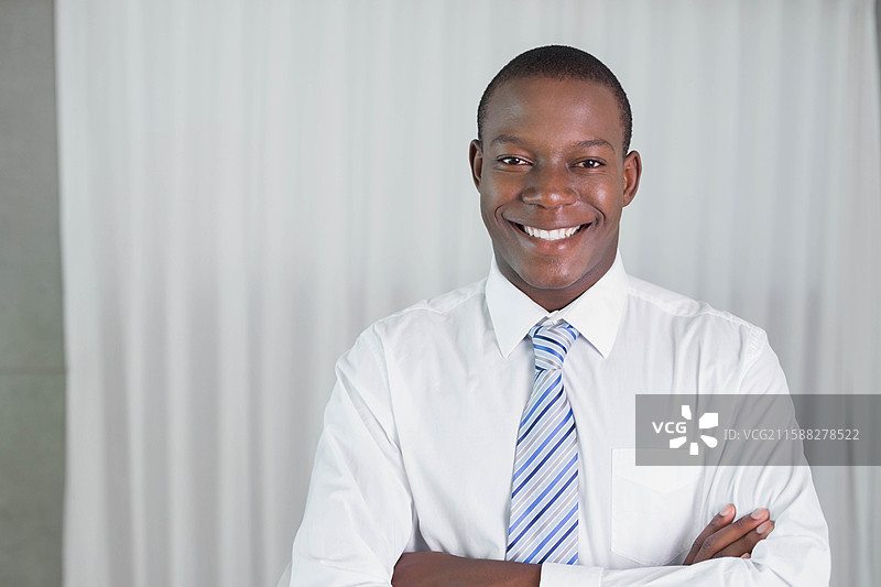 非裔美国商人在窗帘前站立，穿着白衬衫和浅蓝色条纹领带。图片素材