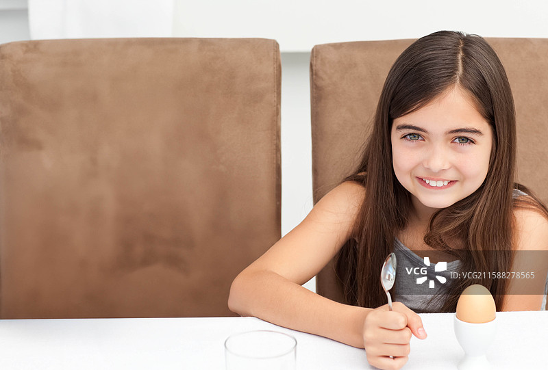 女童坐在餐桌旁，手持勺子，准备吃软煮蛋和一杯饮料，留有空白空间。图片素材
