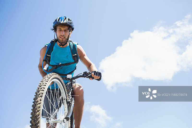 男子在户外骑山地自行车做单轮骑行，穿着骑行衫，头戴头盔，天空晴朗。图片素材