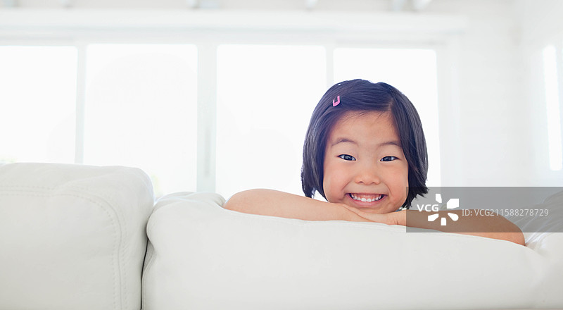 亚洲女孩在客厅的沙发上靠着窗户，脸上洋溢着笑容，头上别着粉色发夹。图片素材