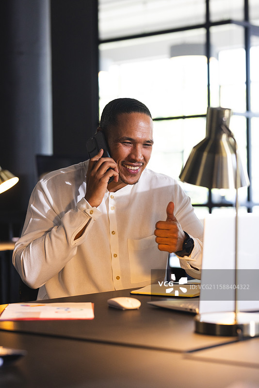 微笑的男人在办公室桌子旁打电话并竖起大拇指图片素材
